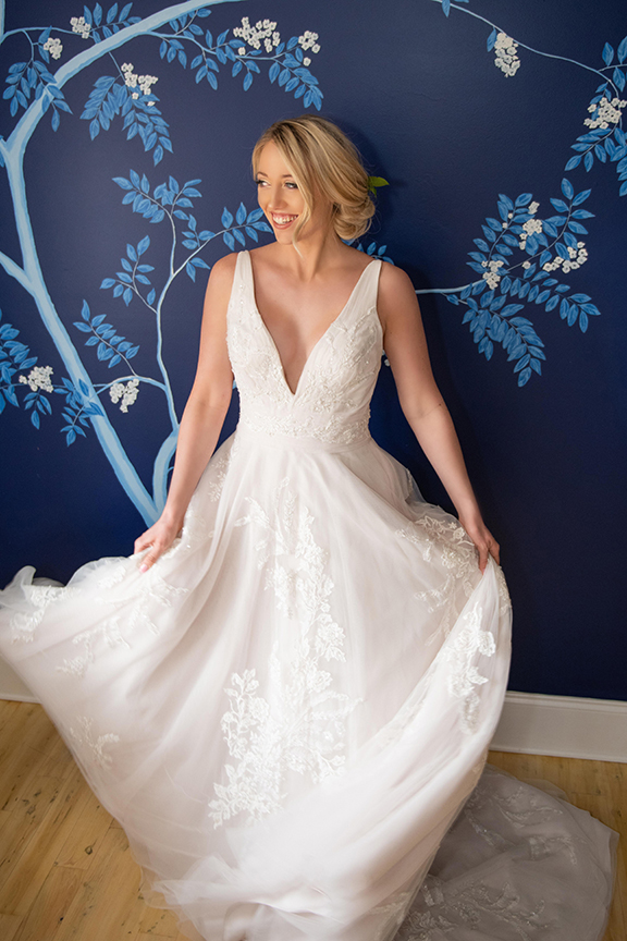 beautiful bride in stunning low cut wedding dress, wedding hair softly pulled back, on a handpainted blue wall in Oakleaf Cottage